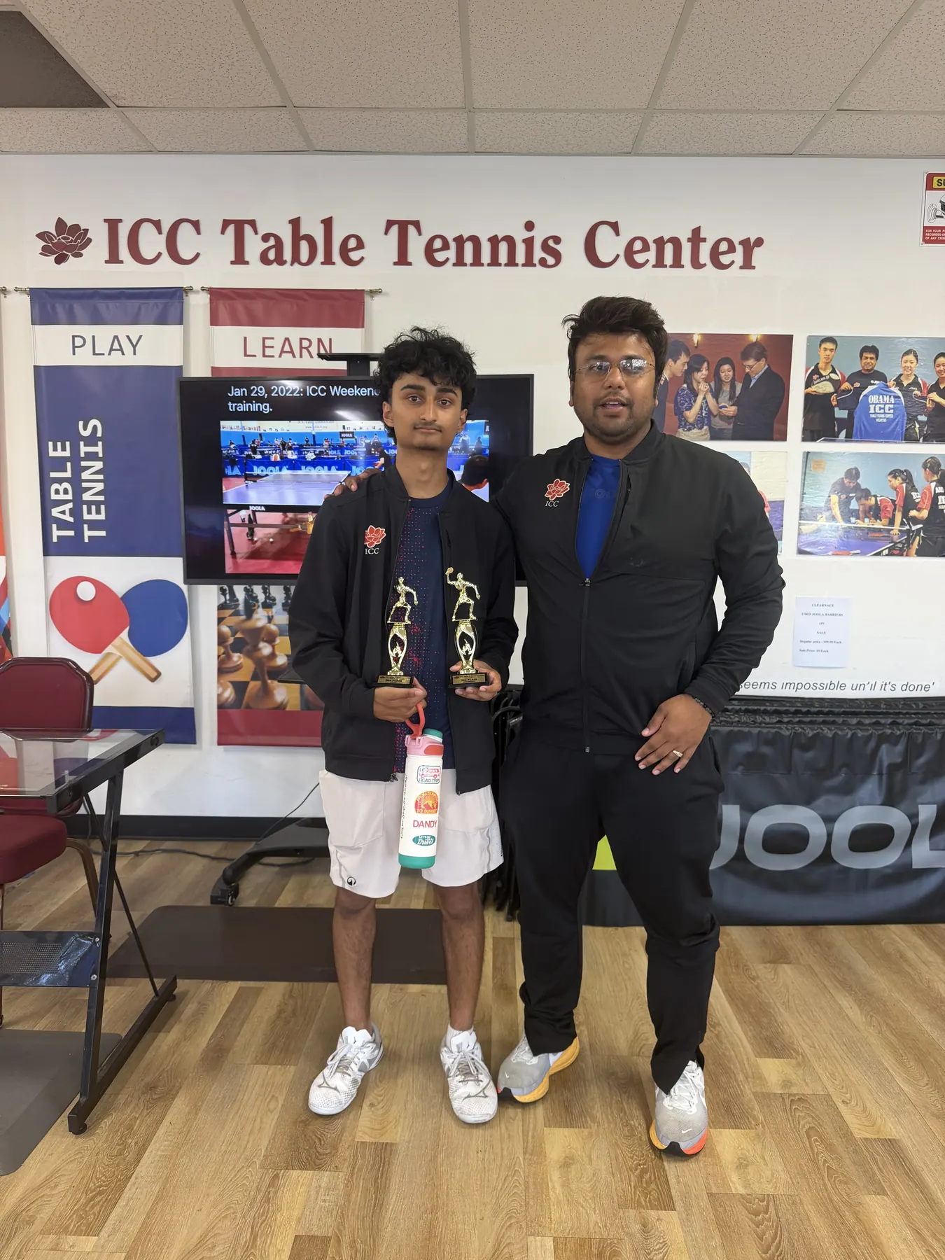 Keshav Sridhar and Subham Kundu holding trophies under the ICC Table Tennis Center sign