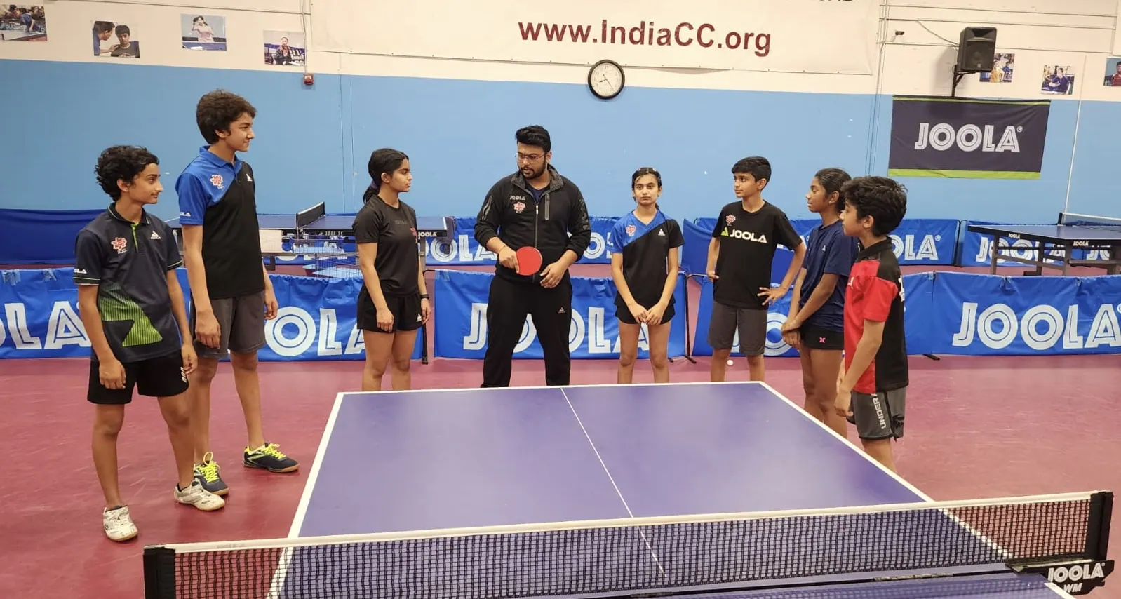 Subham Kundu coaching a group of young players around a table at ICC Table Tennis Center